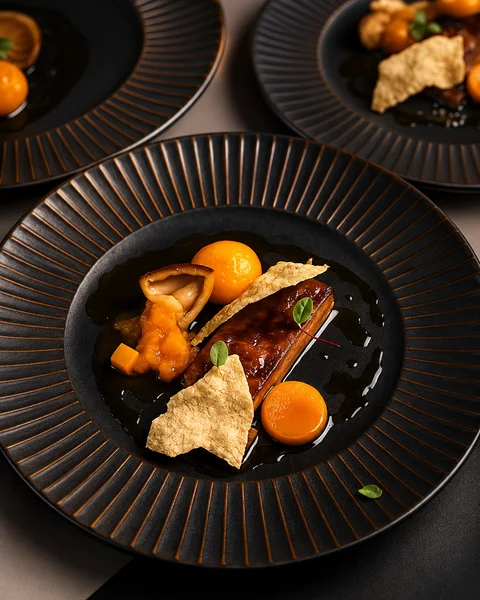 A plated dish with orange purée on a black plate