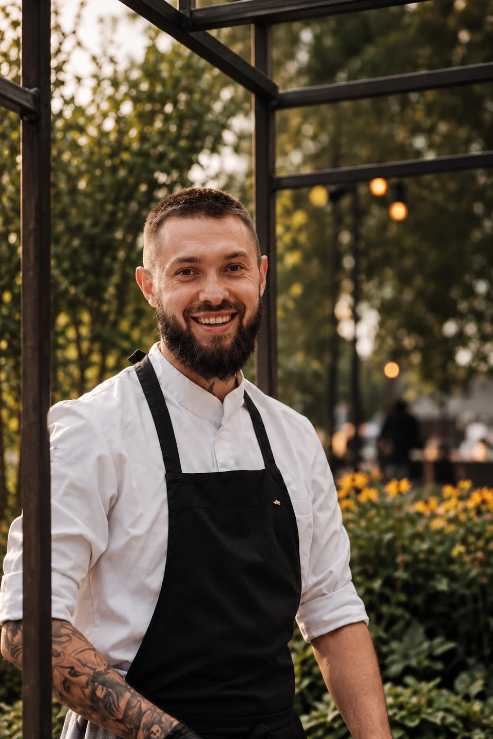 Chef Petre smiling in a white chef jacket and black apron outdoors.